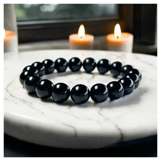 Black beaded bracelet on a marble surface with candles in the background